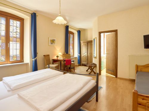 Helles gemütliches schlafzimmer mit betten tisch stuehlen kleiderschrank und fenstern mit blauem vorhang