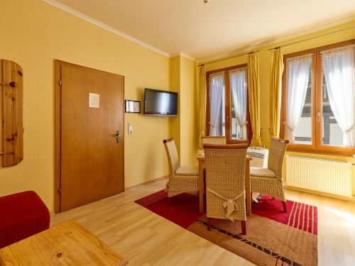 Helles wohnzimmer mit holztisch und sesseln rotem teppich fenstern mit gardinen und wandhalterung fernseher