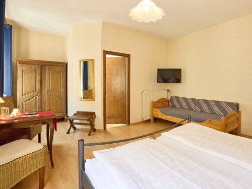 Hell eingerichtetes hotelzimmer mit bett kleiderschrank tisch sessel und sofa vor gelben wanden