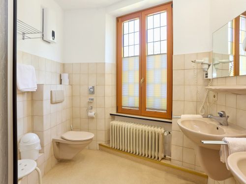 Helles Badezimmer mit Toilette Waschbecken Handtucher Foner Spiegel Fenster und Heizkorper