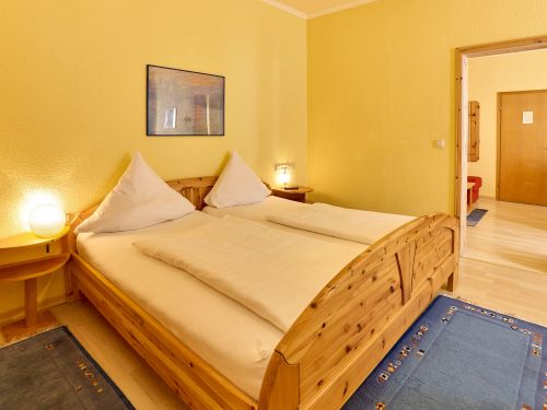 Schlafzimmer mit gelben Wänden Holzbett zwei Nachttischen mit Lampen und blauen Teppichen auf dem Boden