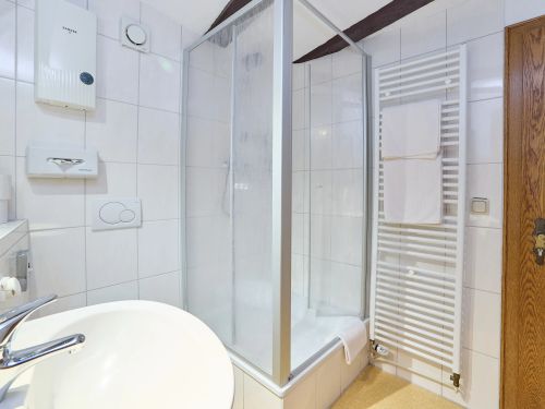 Kleines Badezimmer mit Dusche Handtuchheizkörper Waschbecken und Holztür in weiß gekacheltem Raum