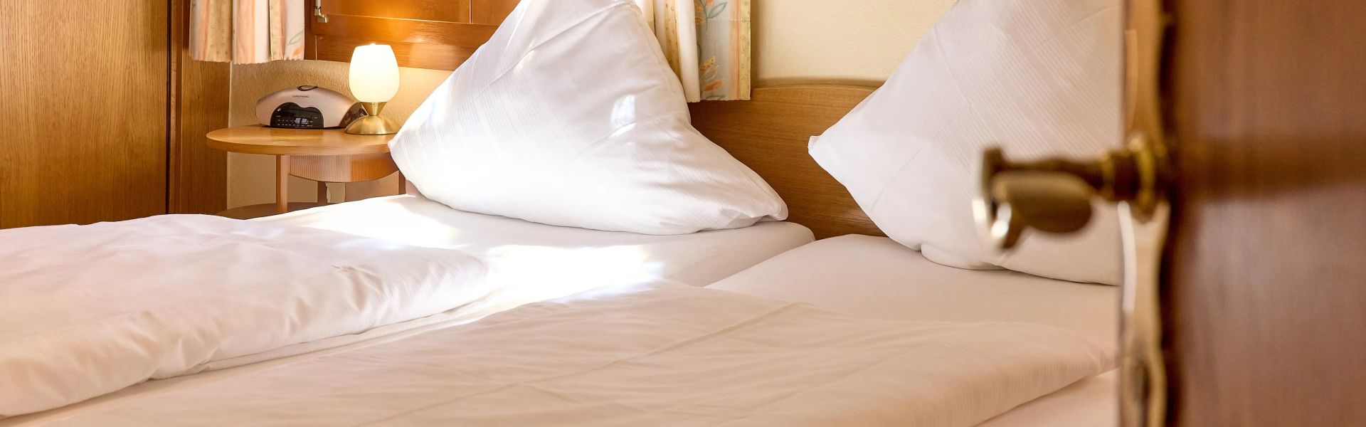 Gemütliches Doppelbett mit weißen Kissen und Decken im hellen Schlafzimmer mit Holzmöbeln und Fensterlicht