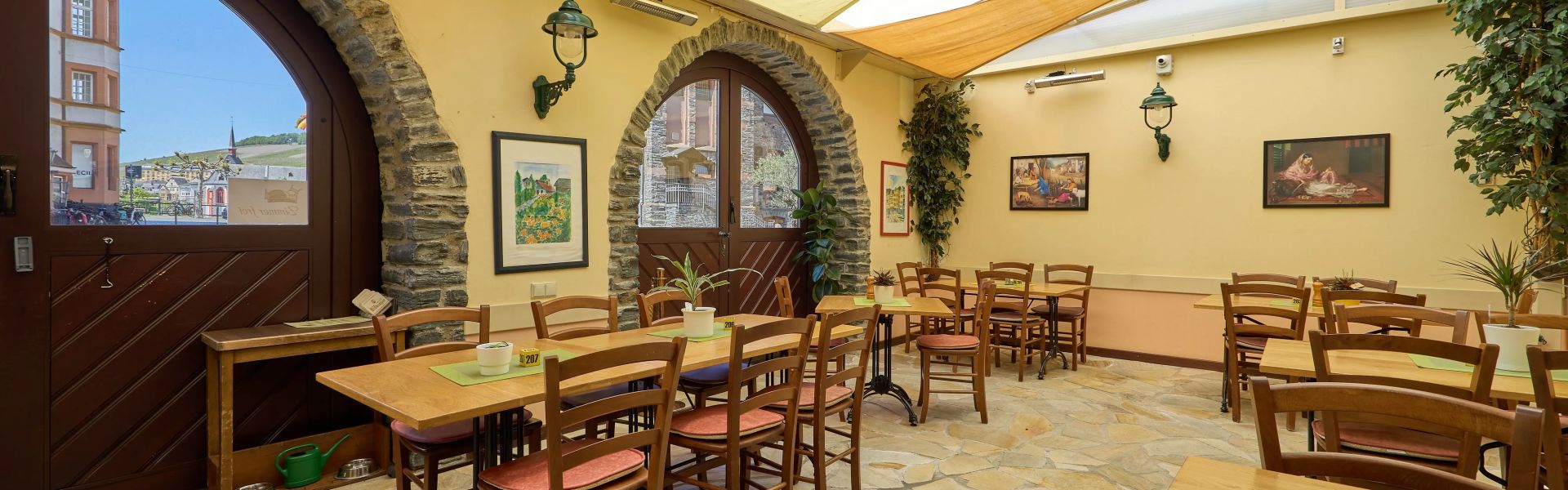 Helles gemütliches Restaurant mit Holzmöbeln Steinboden und großen Fenstertüren mit Sicht nach draußen